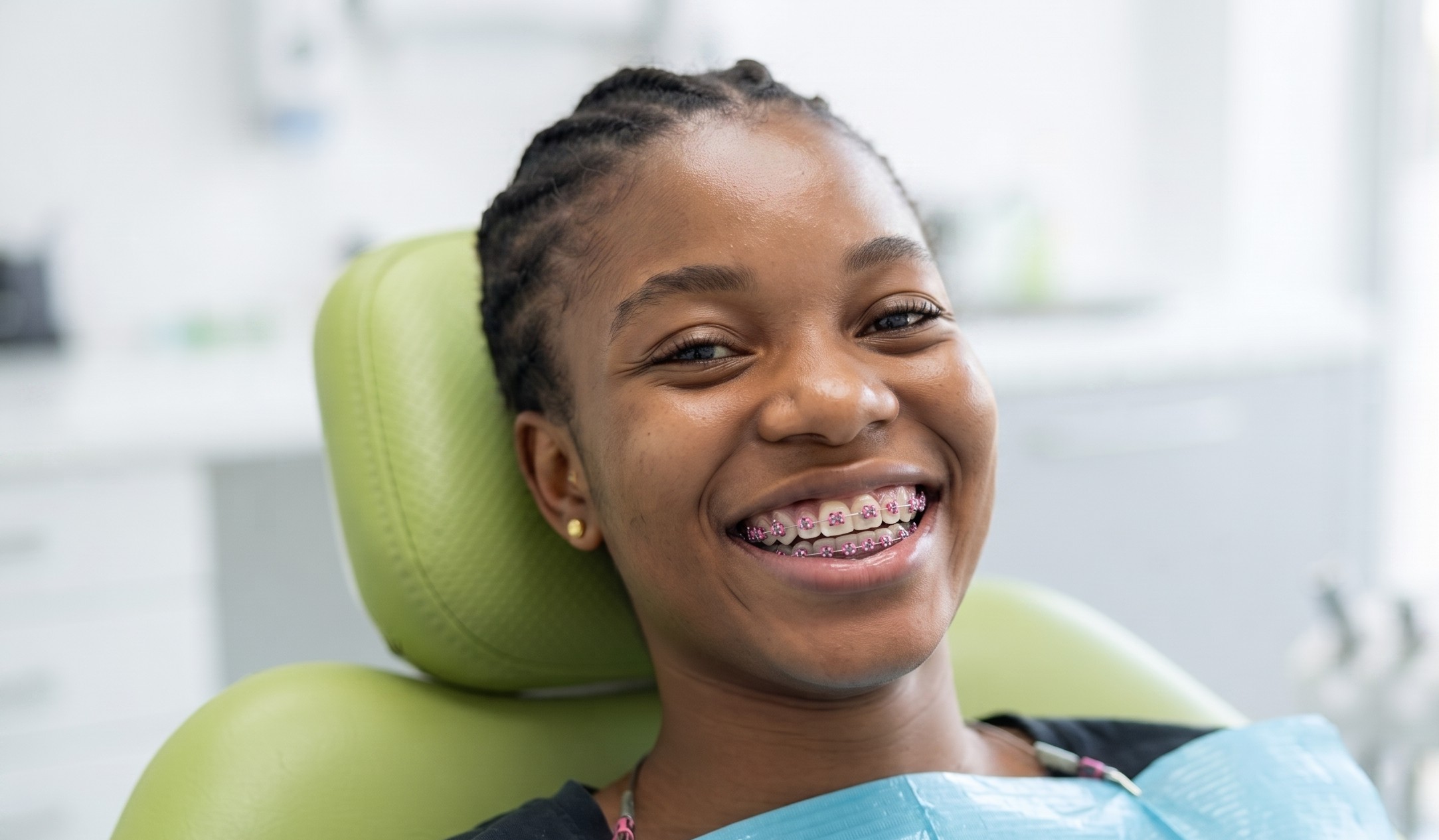 A young woman smiling with braces while seated in the dental chair at her orthodontic review